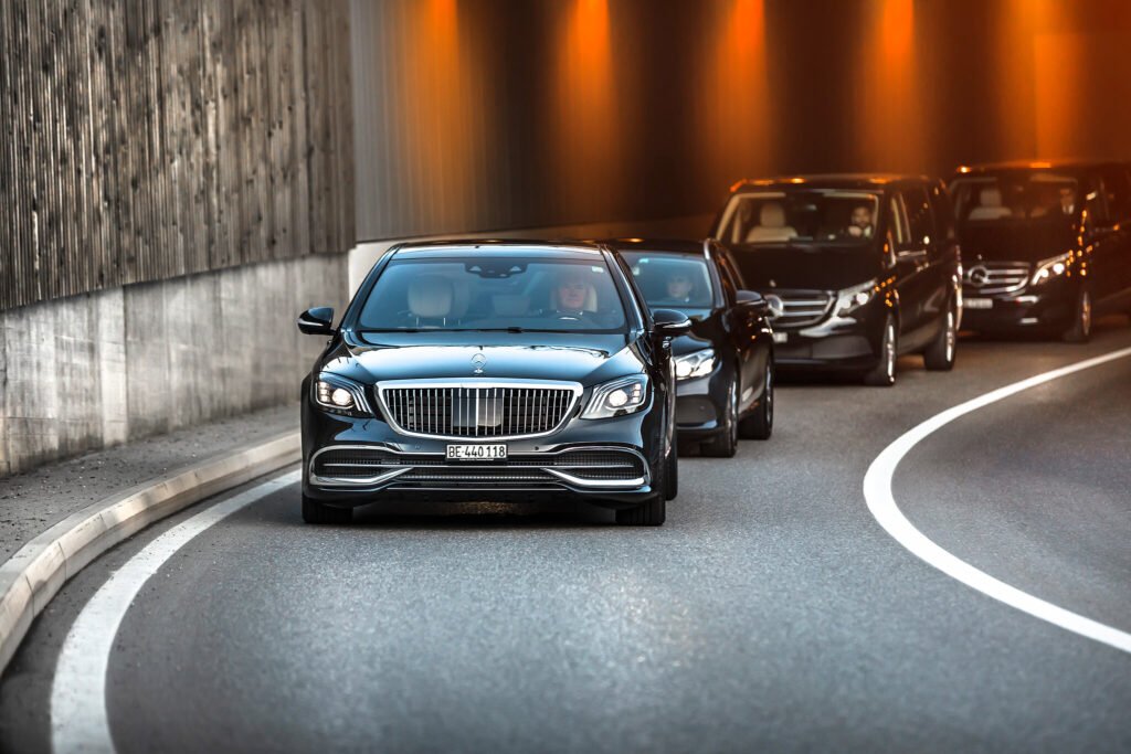 "A convoy of black luxury vehicles, led by a Mercedes-Maybach S-Class with the license plate 'BE-440 118,' drives through a tunnel."
