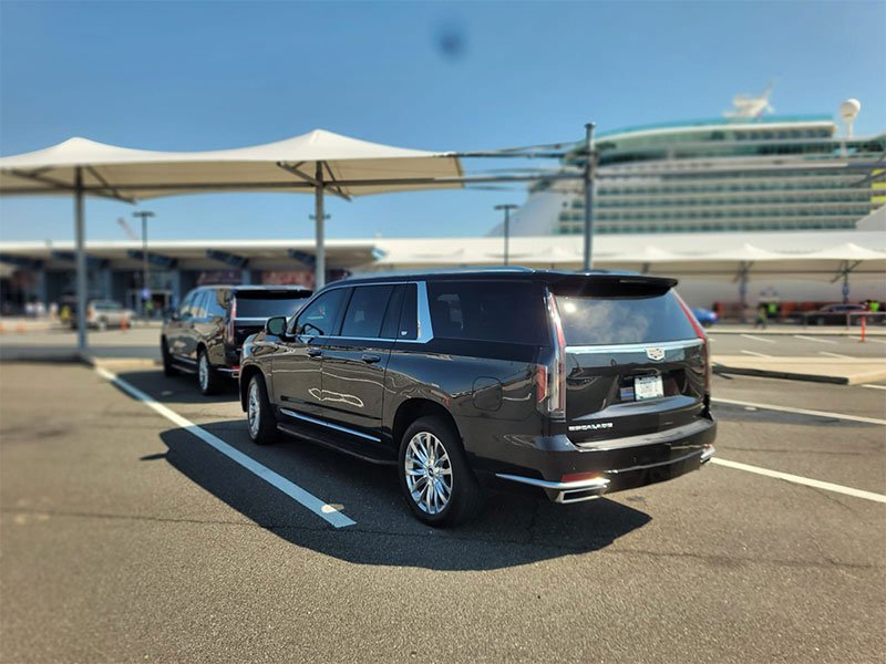 "A black Cadillac Escalade ESV parked in a lot with a large white cruise ship in the background under a clear blue sky."