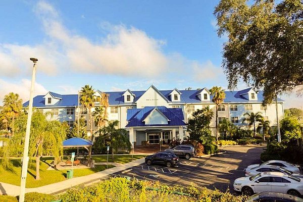 White and blue multi-story Seffner Inn and Suites with dormer windows, surrounded by palm trees and greenery; parking lot with cars in front under a blue sky with white clouds.