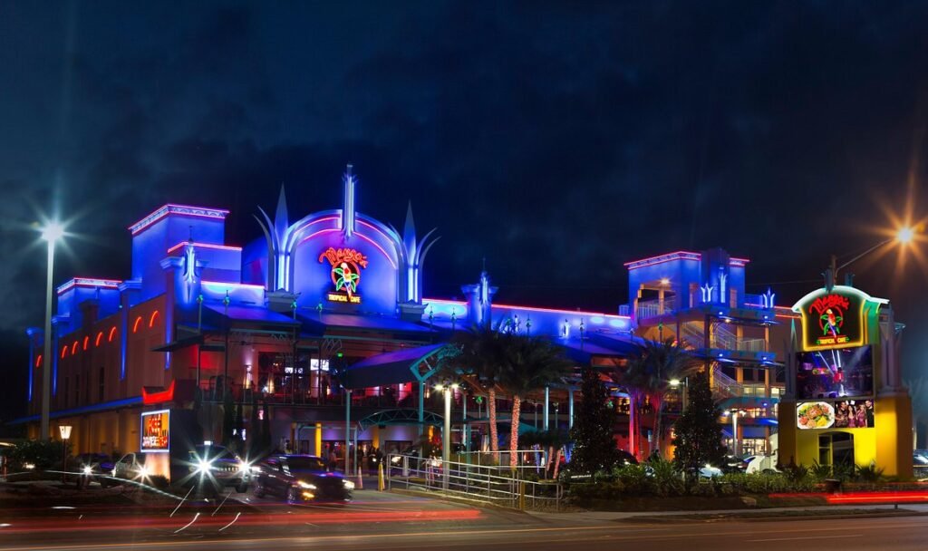 Mango's Tropical Cafe in Orlando at night, glowing with vibrant blue and pink neon lights, with streetlights and light trails from passing cars in the foreground.